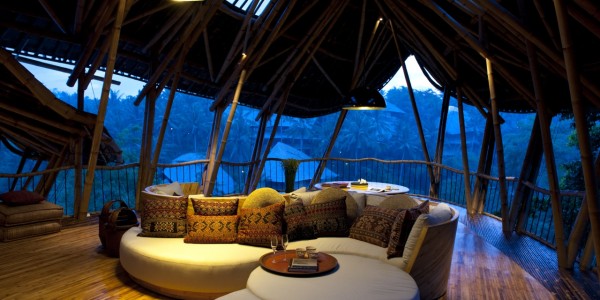 The fourth-floor living room of Sharma Springs with the Ayung river valley and the rooftops of Green Village beyond.  Yin-Yang sofa looks both inward and outward in this  spacious open-air living room. Brass bowl lamps suspended above.  Traditional Indonesian Ikat cushion covers.  Photographed at dusk. 
Flooring is golden bamboo hand-laid onsite with brass nails. 

Structure primarily dendrocalamus asper 'Petung' bamboo. Naturally brown fargesia robusta 'Wolong' bamboo rafters and accents. 


Sharma Springs, a private home designed for and belonging to Sumant and Myriam Sharma and their four daughters. 
Located on the Ayung River valley, Sibang, Bali, Indonesia.
Architecture by Ibuku.
Custom furniture design by Ibuku.
Bamboo sourcing, treatment and construction by PT Bamboo Pure.
Interior design by Yajaira Smyth and Elora Hardy.
Antiques selected by Yajaira Smyth.
Photograph by Rio Helmi, July 2013.
Styling by Elora Hardy & Yajaira Smyth. 
Completed in July 2013.